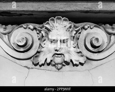 Decorative detail on the facade. Relief on the facade of a building. Stucco molding in the form of a man's head with curly hair, mustache and curls on the sides. High relief concrete bas-relief. Stock Photo