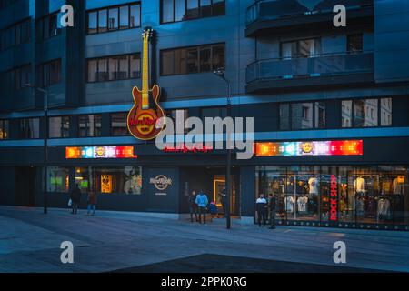People at Hard Rock Caffe with big neon guitar and shop display in capital city of Andorra Stock Photo