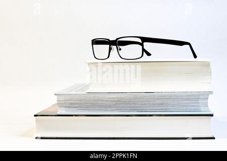 three thick books on a table with glasses as a visual aid and a white background Stock Photo