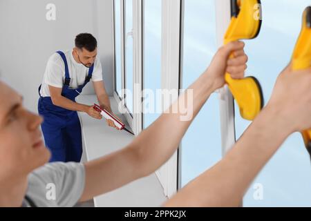 Workers with tube of sealant and suction lifters installing plastic windows indoors Stock Photo