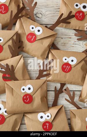 Set of gifts in envelopes with deer faces on white wooden table, flat lay. Christmas advent calendar Stock Photo