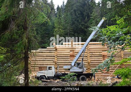 The process of building a wooden house from wooden beams of cylindrical shape. Crane in working condition Stock Photo