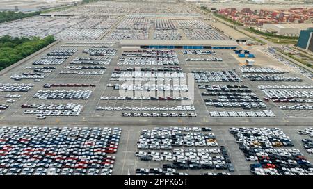 Aerial view of new cars stock at factory parking lot. Above view many cars parked in a row. Automotive industry. Logistics and supply chain business. Import or export new cars at warehouse near port. Stock Photo