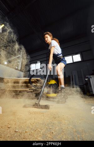 Young woman using vacuum cleaner in a carpentry workshop Stock Photo