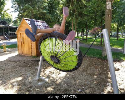 Sremska Mitrovica, Serbia, 13 September 2020. Children swing on a spider-web swing. Boy and girl, brother and sister in the summer on the playground. Swinging the swing Stock Photo