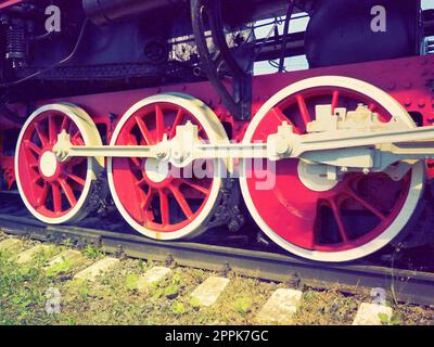 Retro vintage wheels of a locomotive or train close up. Red large heavy metal wheels with piston guiding mechanisms. Locomotive of the 19th - 20th centuries with a steam engine. Retro style Stock Photo