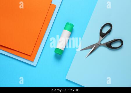 Glue stick, scissors and colorful paper on light blue background, flat lay Stock Photo