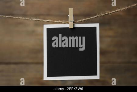 Clothespin with empty instant frame on twine against wooden background. Space for text Stock Photo