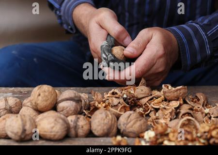 Man cracking walnuts at wooden table, closeup Stock Photo
