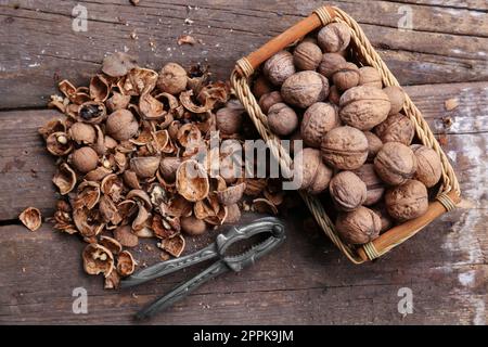 Walnuts, pieces of shells and nutcracker on wooden table, flat lay Stock Photo