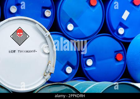 Old chemical barrels. Blue and green oil drum. Steel and plastic oil tank. Toxic waste warehouse. Hazard chemical barrel with warning label. Industrial waste in drum. Hazard waste storage in factory. Stock Photo