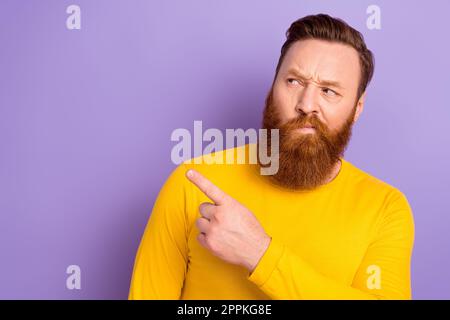 Photo of young virile man red beard distrust direct finger empty space looking expensive prices shop isolated on purple color background Stock Photo