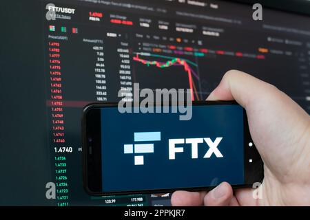 Man holding phone with FTX logo. Global fall of cryptocurrency graph - FTT token fell down on the chart crypto exchanges on app screen. FTX exchange bankruptcy and the collapse depreciation of token. Stock Photo