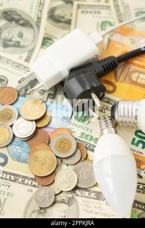 The concept of the energy crisis, price increases. Euro and dollar banknotes, coins on the background of a lamp, plug, cord. Tax time, bill payment, calculator for counting. Vertical photo. Stock Photo