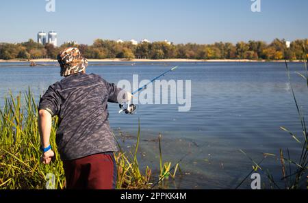 A male fisherman threw a spinning rod into a lake or river on a sunny day.