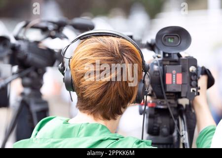 Camerawoman at work during news conference or media event filming with video camera Stock Photo