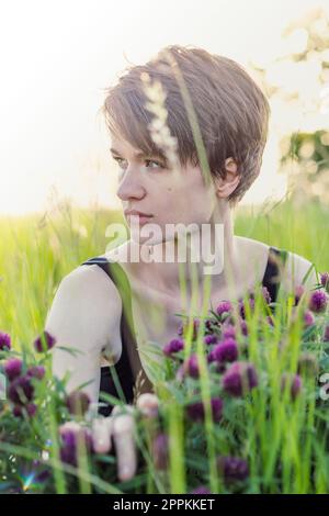 Close up thoughtful lady sitting in fresh grass portrait picture Stock Photo