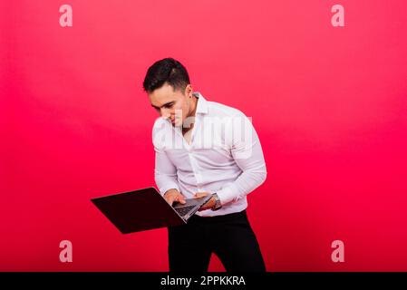 Image of young cheerful businessman in watch holding and using laptop isolated over red background Stock Photo