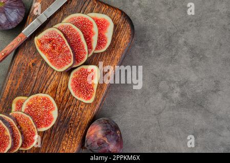 Wooden board with fresh figs cut into slices and an old knife on a gray kitchen table, top view with copy space. seasonal ripe fruits, mediterranean d Stock Photo