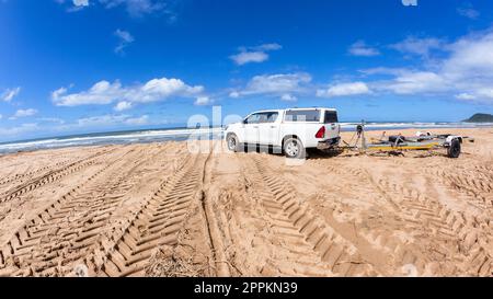 Empty vehicle boat trailer on beach sand along waters edge  with boat owners gone fishing  in the  ocean sea landscape. Stock Photo