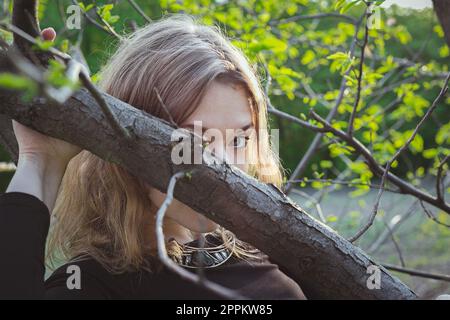Close up young woman peeking over tree bough portrait picture Stock Photo