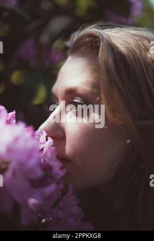 Close up woman smelling flowering shrub with pink flowers portrait picture Stock Photo