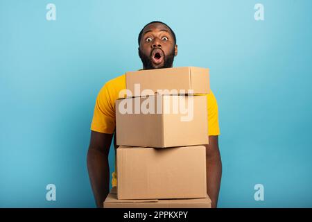 Man receives a lot of packages and has a surprised expression. Cyan background Stock Photo