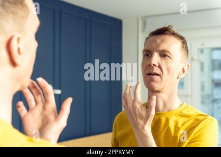 Middle aged man apply moisturizing cream with finger on clear facial areas. Male portrait in mirror. Skincare concept. Stock Photo