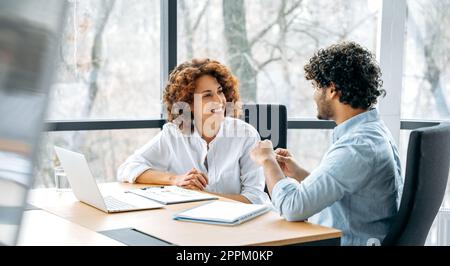 Panoramic photo of two friendly colleagues of the company, african american woman and indian man, working together on a new project in modern office, together discussing ideas and goals, communicating Stock Photo