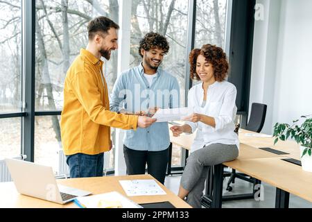 A group of multiracial business people, colleagues at work, looking through documents in a modern office, analyzing financial statements, satisfied with the results, smiling, discussing prospects Stock Photo