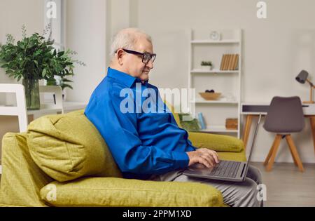 Focused elderly man sitting on sofa using laptop Stock Photo