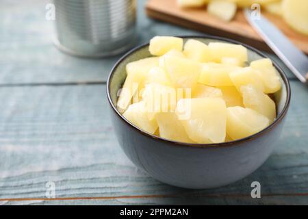 Pieces of delicious canned pineapple in bowl on light blue wooden table, closeup Stock Photo