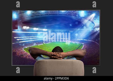 Viewer in front of a large TV relaxed on the armchair at home watching a sports game Stock Photo