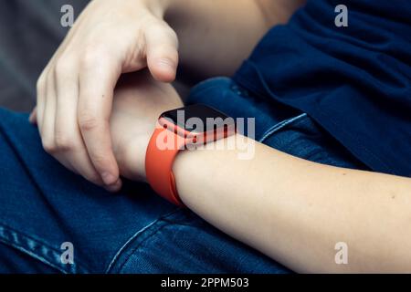 Red stylish smart watch on male wrist closeup. Touch finger on empty screen of wearable gadget to look time and data. Stock Photo
