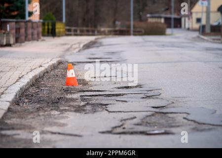 Damaged asphalt pavement road with potholes and traffic cone Stock Photo