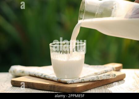 Pouring tasty fresh milk from bottle into glass on white wooden table, closeup Stock Photo