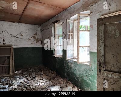 Scary windows. Inside an abandoned house. View of broken windows without a curtain. Grunge scene. Light shines through old wooden frames with broken glass. The concept of abandonment and uselessness. Stock Photo