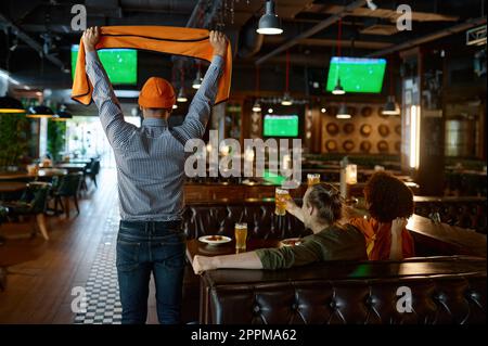 Young excited overjoyed friends watching football match in sports bar Stock Photo