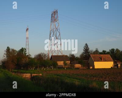 House and arable land next to the power line. Electrical network, power equipment system for the transmission of electricity by means of electric current. Negative effects of electromagnetic radiation Stock Photo