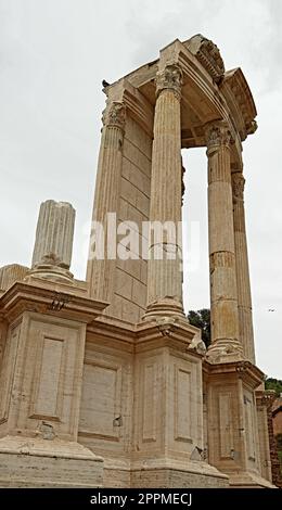 An aged Roman temple in ruins, with crumbling pillars, arches and walls covered in ivy and other foliage Stock Photo