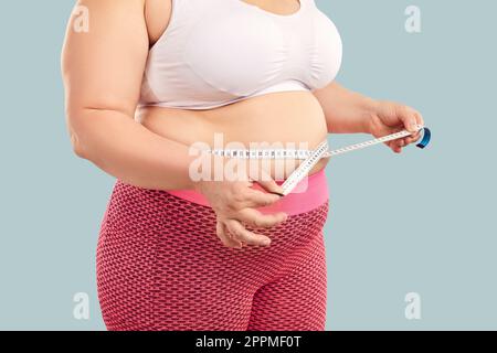 Overweight woman with a big fat abdomen measures her waist with a centimeter tape Stock Photo