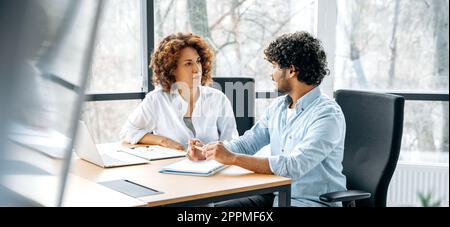 Panoramic photo of two focused employees of the company of different nationalities are working together on a new project in a modern office, together discussing ideas and goals, communicating Stock Photo