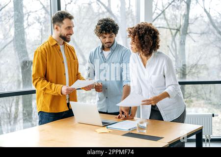 Friendly multiracial business partners gathered in meeting room, confident businesspeople discuss new project, creative ideas, promotion strategy, analyze financial risks and profits, smile Stock Photo