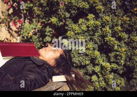 woman lying and sleeping on a wooden table with a book Stock Photo