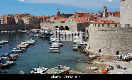 Dubrovnik, Croatia, August 14, 2022. City port in summer, tourist attraction. Tourists walk, get into boats and ships and go on boat trips. Adriatic Sea. A local resident plays with a dog. Old forts. Stock Photo