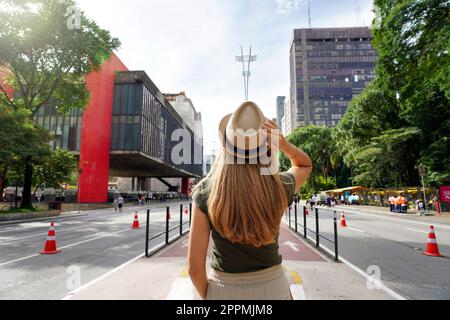 Visiting Sao Paulo City, Brazil. Rear view of beautiful tourist woman with hat walking along Paulista Avenue, Sao Paulo, Brazil. Stock Photo