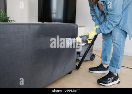Man dry cleaner's employee hand in protective rubber glove cleaning sofa with professionally extraction method. Early spring regular cleanup. Commercial cleaning company concept Stock Photo