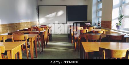 Music solfeggio empty class at school. The sun's rays fall on the floor through the window. Wooden student tables and chairs. School board and white walls. School interior. Stock Photo