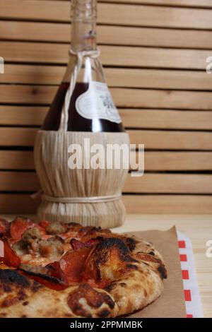 Fresh Pizza on Wooden Table at Restaurant With Bottle of Chianti Wine in Background Stock Photo