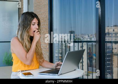young entrepreneurial colombian latina woman, with her laptop sitting working at home surprised by her economic gains, business concept, copy space. Stock Photo
